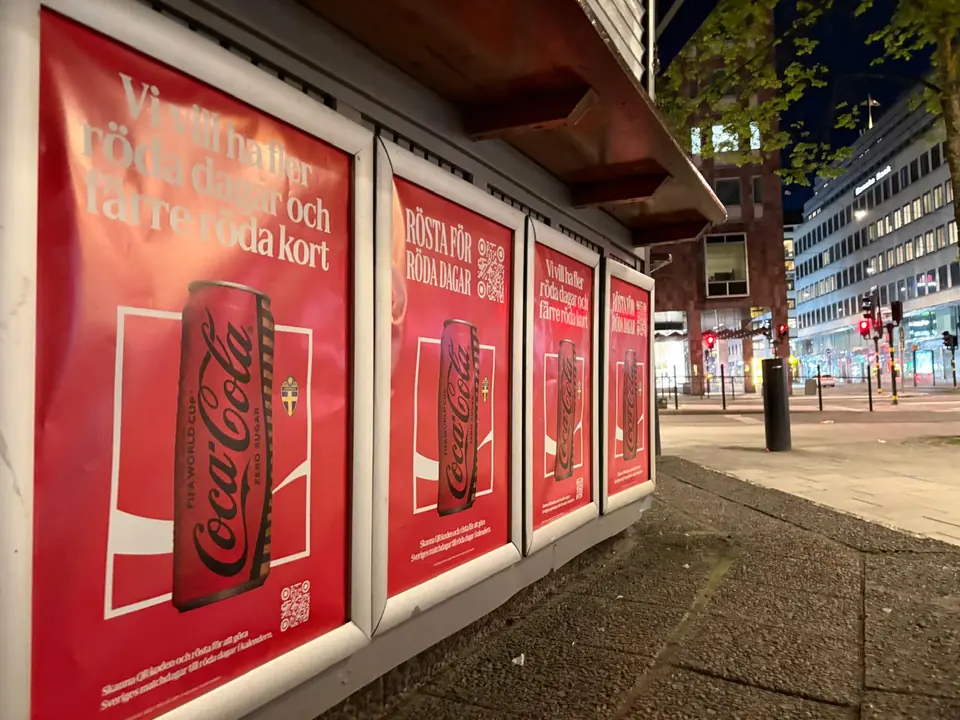Fyra röda Coca-Cola Zero-affischer i ramar på en kiosk i Stockholms city på kvällen