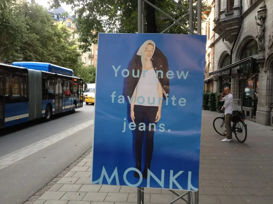 Monki-plakat Your new favourite jeans på et stativ ved et busstoppested i Stockholm